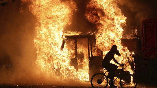 A man on a bike rides past a city truck as it burns outside the Kenosha County Courthouse. 