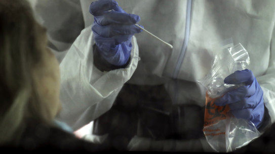 A nurse prepares to take a sample for a COVID-19 test .