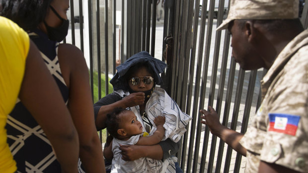 A Haitian police asks a woman to move away from a gate at the US Embassy in Port-au-Prince, Haiti.