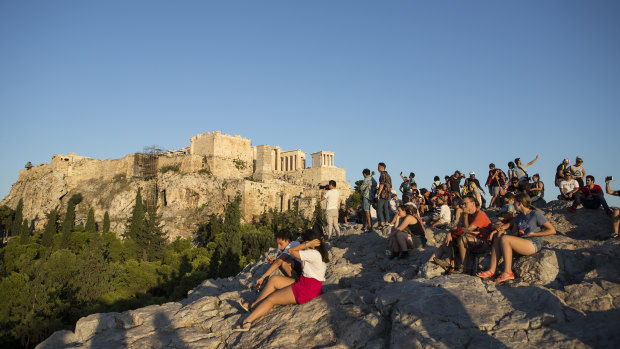 Tourists sit under the Parthenon and watch the sunset over Athens.