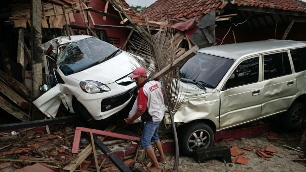 A man clears debris in front of damaged cars and buildings at the Villa Avi Redita in Carita.