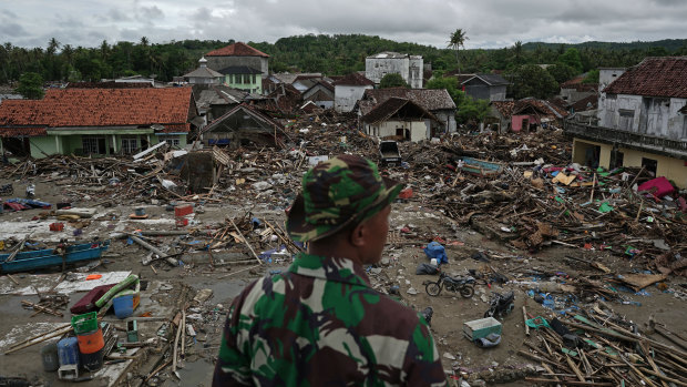 An Indonesian soldier looks at damaged houses and debris in Sumur.