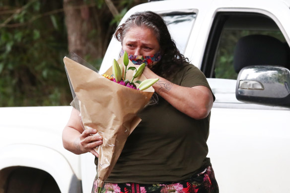 A member of the public holding a bouquet of flowers outside the home where twin four-year-old girls died following a house fire in Goonengerry, west of Byron Bay. 