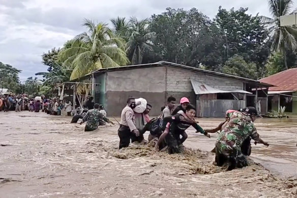 Soldiers and police officers assist residents to cross a flooded road in Malaka Tengah, East Nusa Tenggara province, Indonesia, on Monday, April 5, 2021. 