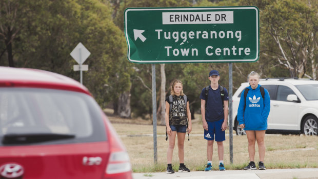 Sisters Cerys Simmons, 12, left, and Rhiannon Simmons, 14, right, wait with classmate Harry, 14, centre, to cross the busy roundabout at the intersection of Erindale Drive and Sternberg Crescent, one of the suggested routes when their school bus is cancelled at the end of April.