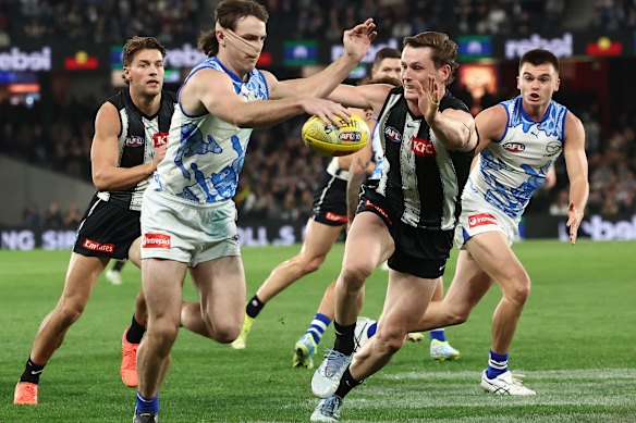 George Wardlaw of the Kangaroos kicks the ball with Ned Long of the Magpies close by.
