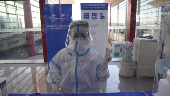 Cheery and covered-up for COVID, a worker poses with “Happy New Year” written on her protective suit at the airport ahead of the 2022 Winter Olympics in Beijing. 
