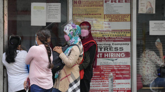 Women stand beside a sign about hiring domestic helpers for the Middle East outside an office in Manila, Philippines. 