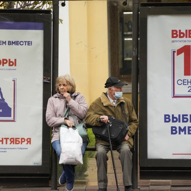 People wait at a St Petersburg bus stop decorated with election posters in September.