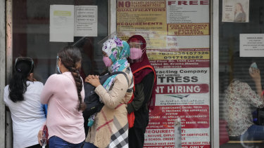Women stand beside a sign about hiring domestic helpers for the Middle East outside an office in Manila, Philippines. 
