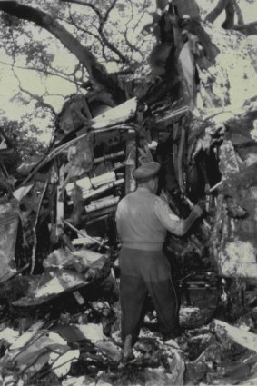 A policeman, trousers wet to his thighs, inspects the aircraft wreckage at Bulwer Island, in which two crew members died.