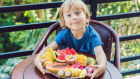 The boy is eating different fruits on the terrace.