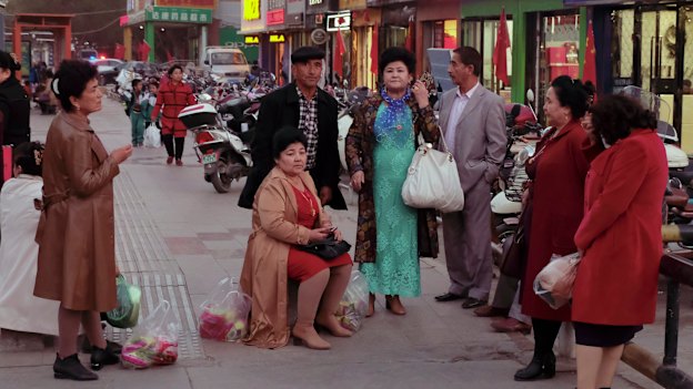A group of older Turpan locals wait, in western dress, in front of a market.