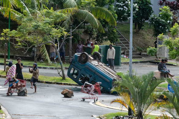 People gather near an overturned car in the Motor Pool district on Tuband in Noumea.
