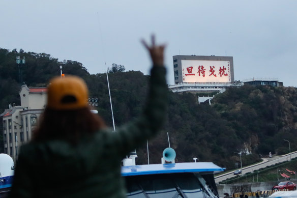 A tourist reacts near a billboard with a message reminding people to be ready to fight on the island of Matsu.