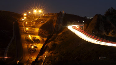 Floodlights from the US illuminate a border wall as traffic flows along a highway in Tijuana, Mexico. 