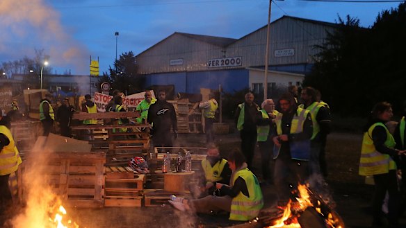Demonstrators stand in front of a makeshift barricade set up by the so-called yellow jackets to block the entrance of a fuel depot in Le Mans, France.