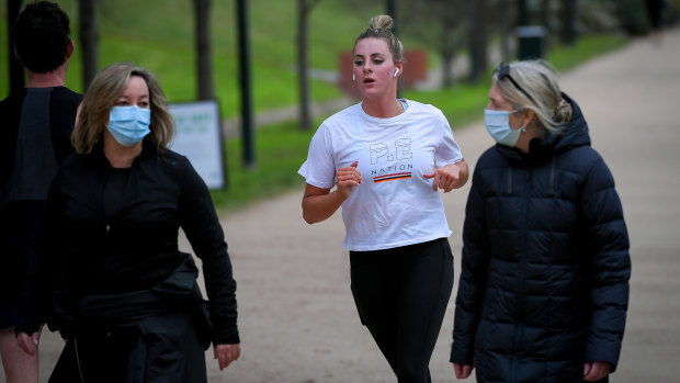 A jogger passes mask-wearing walkers at the Tan on Wednesday.