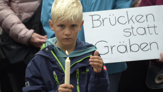 A boy holds candles as he stands in front of a poster reading 'bridges not divisions' during a demonstration for democracy and against extremism in Chemnitz.
