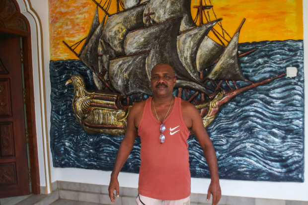 Fernando poses for a photo outside his house, which has a large mural of a ship next to the front door.