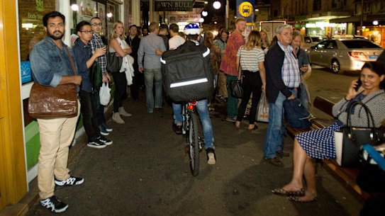 A food delivery cyclist on King Street in Newtown, rides on the footpath through a busy bus stop.