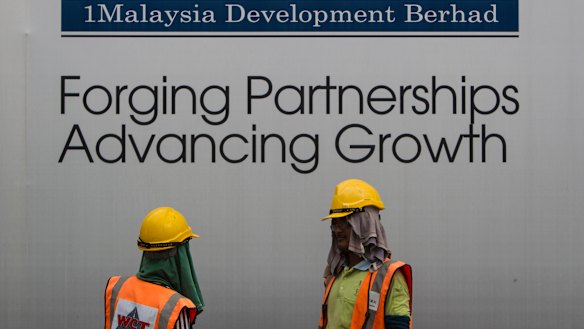 Construction workers chat in front of a billboard for state investment fund 1 Malaysia Development Berhad (1MDB) in Kuala Lumpur, Malaysia.