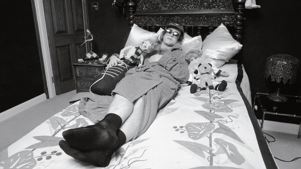 Elton John posing on a bed at his home, mid-1970s. Notice the Elton John doll.