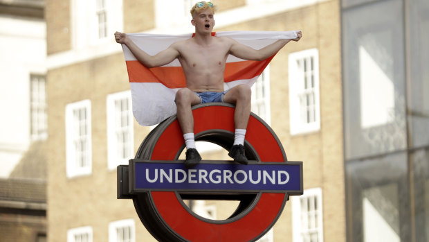 An England soccer fan sits on a London Underground subway sign  after England won their quarterfinal match against Sweden.
