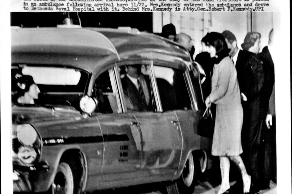 Jacqueline Kennedy, her clothing splattered with blood, watches as the body of the dead president is placed in an ambulance.