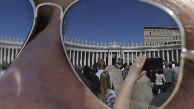The Apostolic palace is reflected on the sunglasses of a man as faithful gather in St. Peter's Square during Pope Francis' Angelus noon prayer at the Vatican.