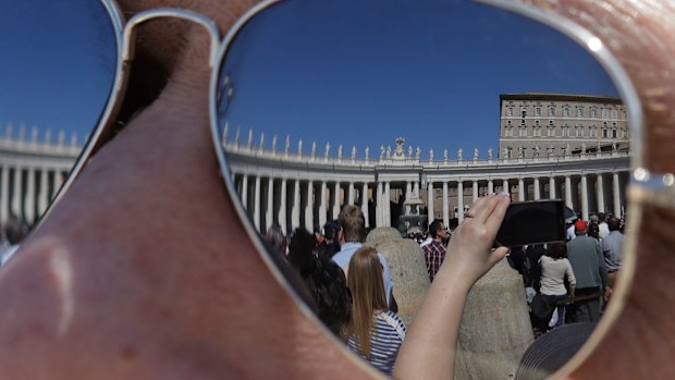 The Apostolic palace is reflected on the sunglasses of a man as faithful gather in St. Peter's Square during Pope Francis' Angelus noon prayer at the Vatican.