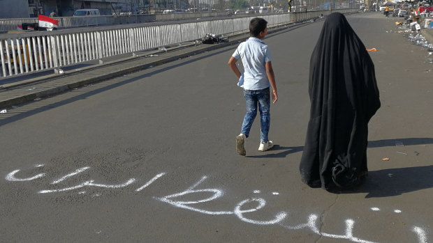 People walk by an Arabic sentence writing on the asphalt reads "Down with Iran" near the site of the protests at Tahrir Square during anti-government protests in Baghdad.