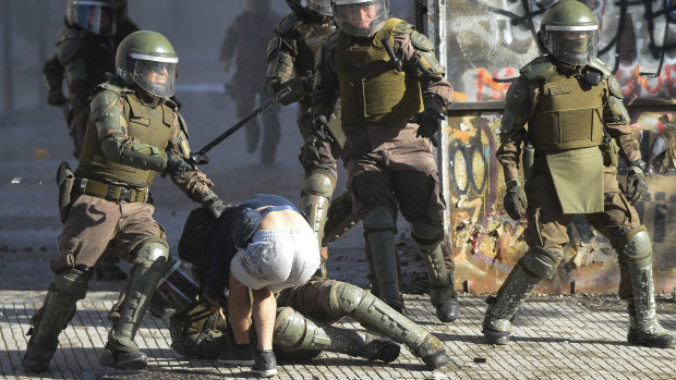 A riot police officer hits a demonstrator during protests against the government of President Piñera on November 27 in Santiago, Chile.