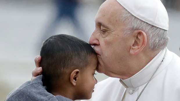 Pope Francis kisses a child as he arrives for his weekly general audience, in St. Peter's Square.