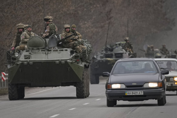 Ukrainian servicemen sit atop armored personnel carriers driving on a road in the Donetsk region.