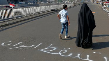 People walk by an Arabic sentence writing on the asphalt reads "Down with Iran" near the site of the protests at Tahrir Square during anti-government protests in Baghdad.