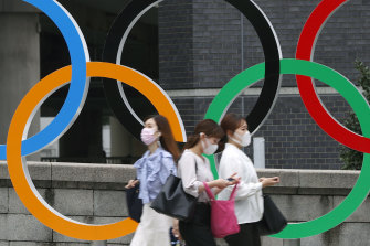 People wearing face masks walk past the Olympics Rings statue in Tokyo.