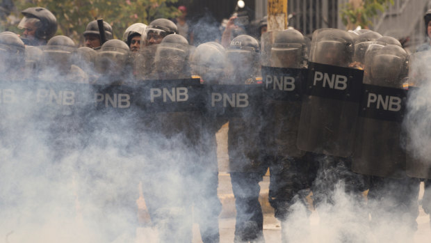 Economic chaos: Riot police stand amid tear gas as they face off with student protesters from the Venezuela Central University in November.