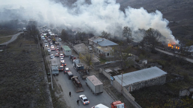 Smoke rises from a burning house as cars and trucks stuck in a huge traffic jam climbing along the road from Kalbajar leaving the separatist region of Nagorno-Karabakh to Armenia.