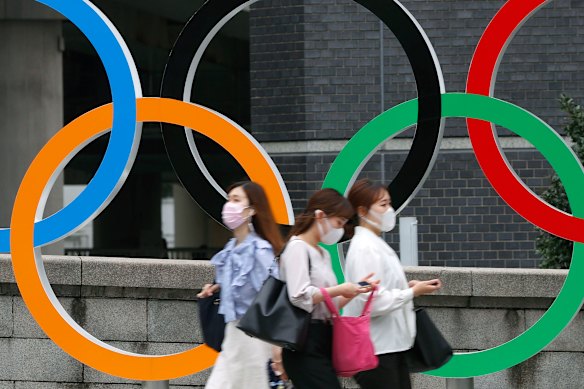 People wearing face masks walk past the Olympics Rings statue in Tokyo.