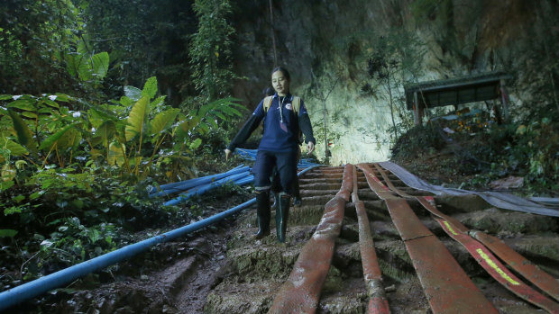 A rescuer makes her way down muddy steps past water pump hoses at the entrance to the cave complex.