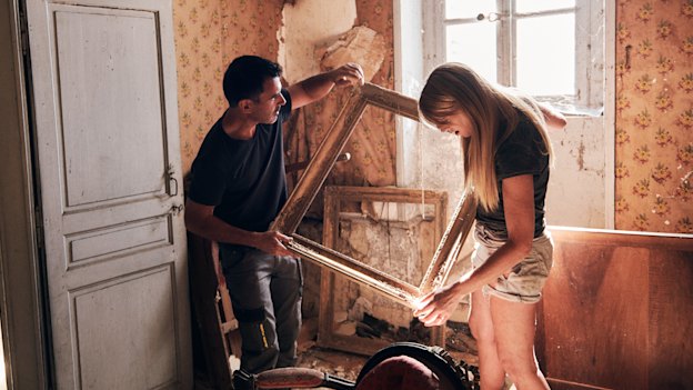 Holding and Selkirk moving picture frames in the water-damaged former staff quarters, a 19th-century chair at their feet. 
