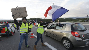 Protesters wearing yellow vests wave a French flag and a poster reading "Free toll" as they open the toll gates on a motorway in Antibes, southern France, on Monday.