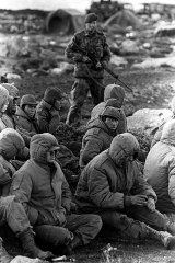 Falkland Adaları'ndaki Goose Green'de yakalanan Arjantinli askerler, bölgeden geçişi beklerken bir İngiliz Kraliyet Deniz Kuvvetleri tarafından korunuyor.