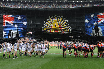 Both teams run through the same banner before the start of the Anzac day match.