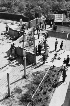 Residents of West Berlin [R], watch East German construction workers erect the wall.