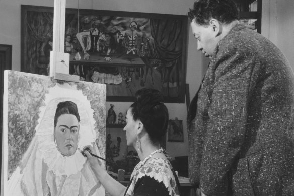 Frida paints a self-portrait while Diego observes her in 1940.