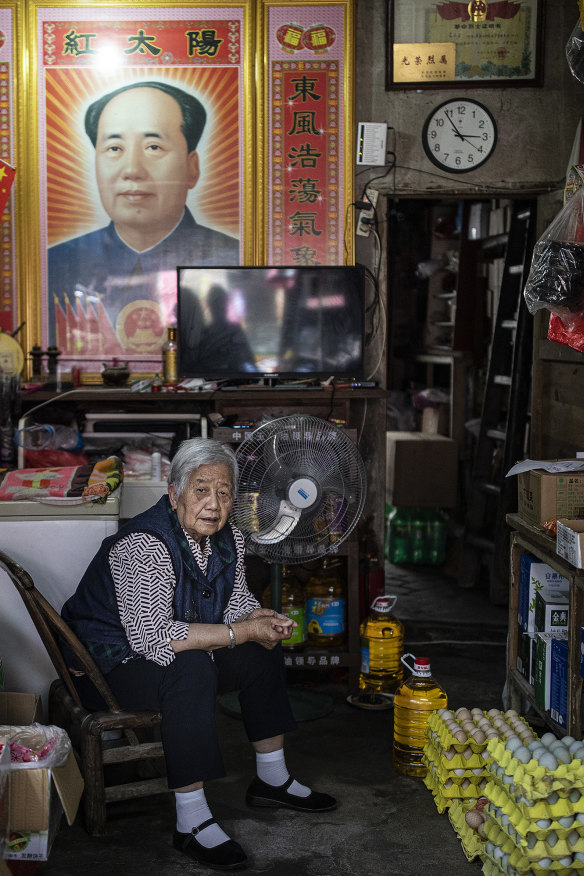 A woman sits in her shop, a poster of Mao hanging behind her, in Hong’an county in June 2021.