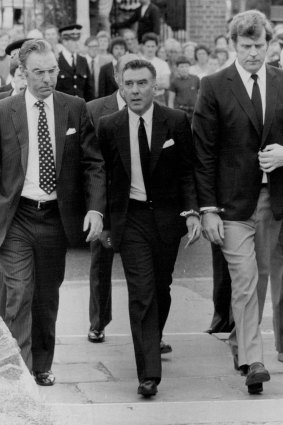 Reggie Kray arrives from Parkhurst handcuffed to a towering officer. 