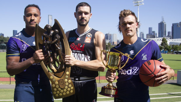 Melbourne Storm forward Felise Kaufusi and Melbourne United skipper Chris Goulding hold the NRL premiership trophy, while Storm’s Ryan Papenhuyzen holds the NBL Cup. 